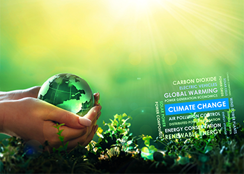 Hand holding glass earth over verdant ground and climate change text.